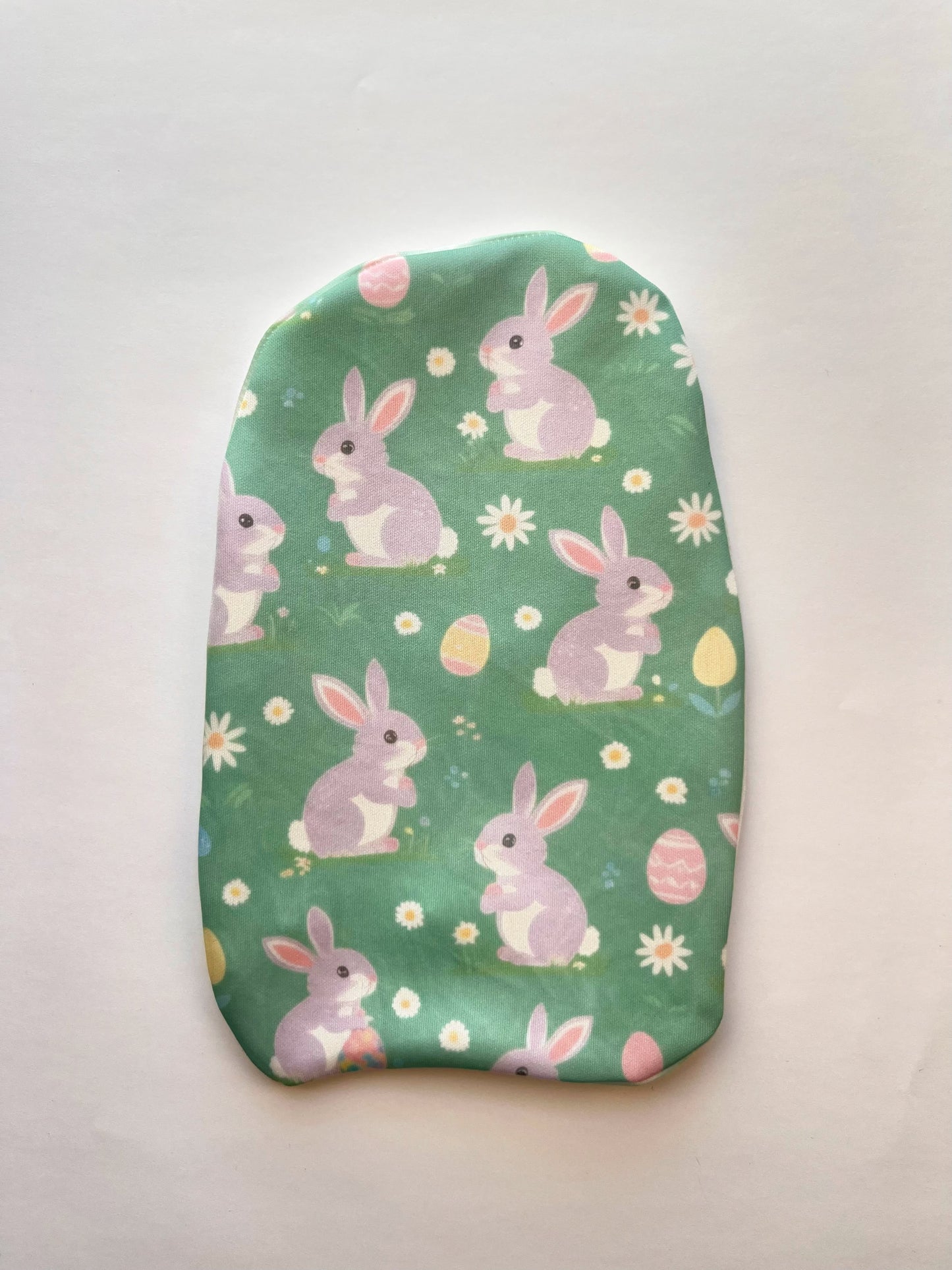 Spring Bunny Dreams stoma bag cover featuring pastel purple Easter bunnies, decorated eggs, and daisies on a soft green background – cute and breathable ostomy pouch cover for Easter or springtime wear.